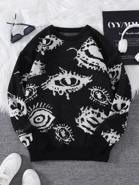 Black sweater with white eye pattern on a gray surface with white shoes and a book in the background.