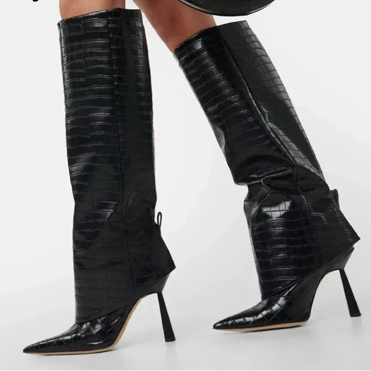 A pair of black knee-high pointed-toe stiletto boots with an embossed crocodile pattern, shown on a model against a light gray background. The brand name 'Eilyken' is visible in the top left corner.