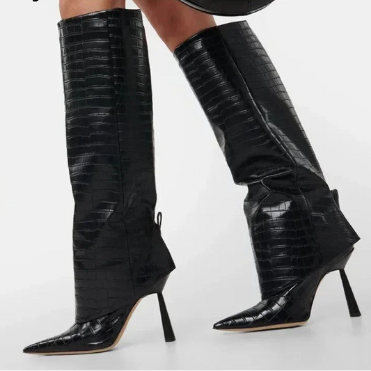 A pair of black knee-high pointed-toe stiletto boots with an embossed crocodile pattern, shown on a model against a light gray background. The brand name 'Eilyken' is visible in the top left corner.