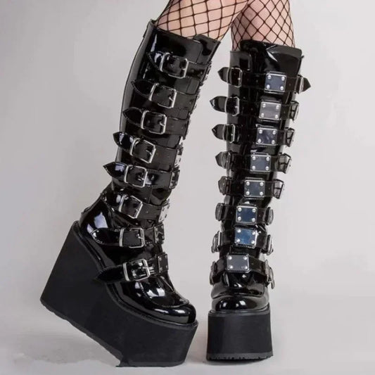 A pair of black patent leather platform boots with multiple buckled straps and fishnet stockings worn with them, shown against a plain light gray studio background.
