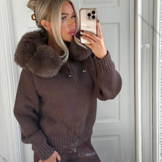 A woman takes a mirror selfie wearing a brown knit zip-up jacket with a large fluffy faux-fur collar. The jacket has ribbed cuffs and hem, and a front zipper with a small metallic pull.