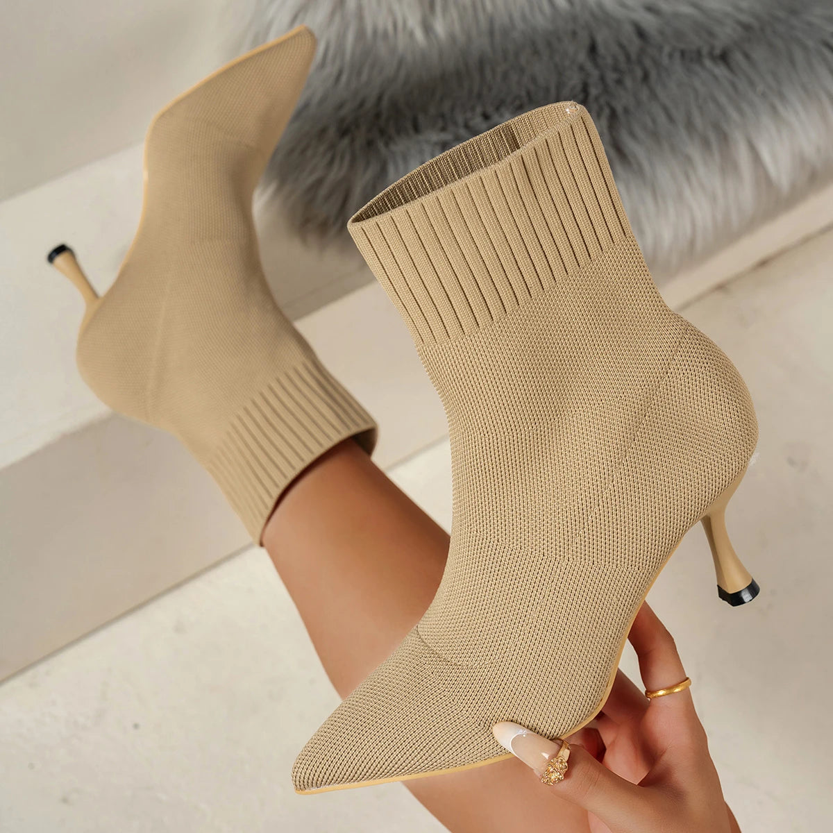 Beige knit ankle boots with high heels held by a hand against a neutral background