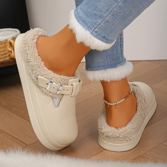 Beige slippers with fur trim worn by a person on a wooden floor.