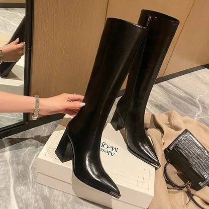 Black knee-high boots on a white box with a beige background