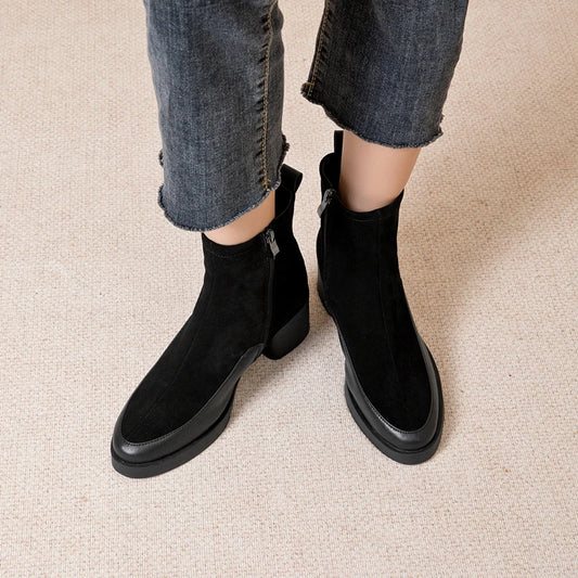 Black ankle boots worn with rolled-up jeans on a beige carpet.