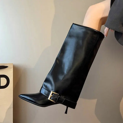 Black knee-high boot with a gold buckle on a neutral background