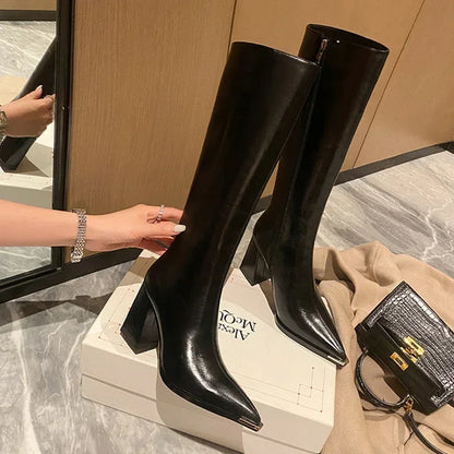 Black knee-high boots on a white box with a beige background
