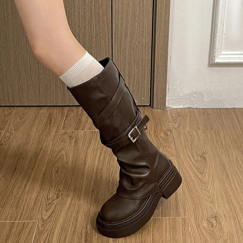 Brown knee-high boot with a buckle on a wooden floor.