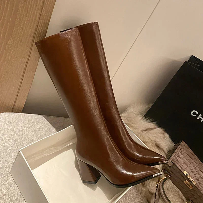 Brown knee-high boots on a light wooden floor with a black handbag and beige bag.