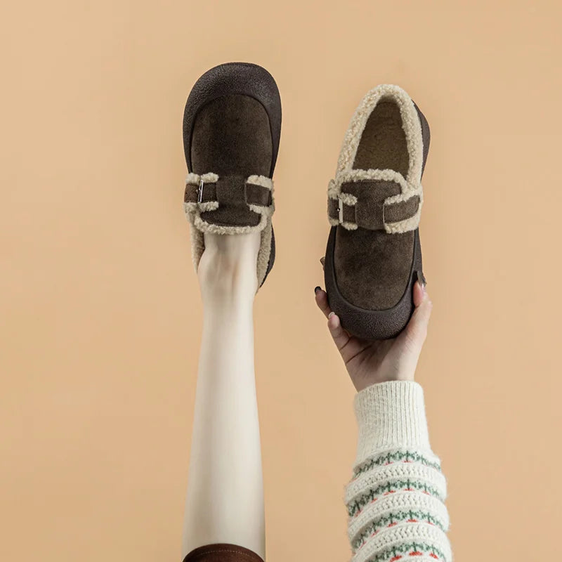 Brown loafers with shearling trim held against a beige background