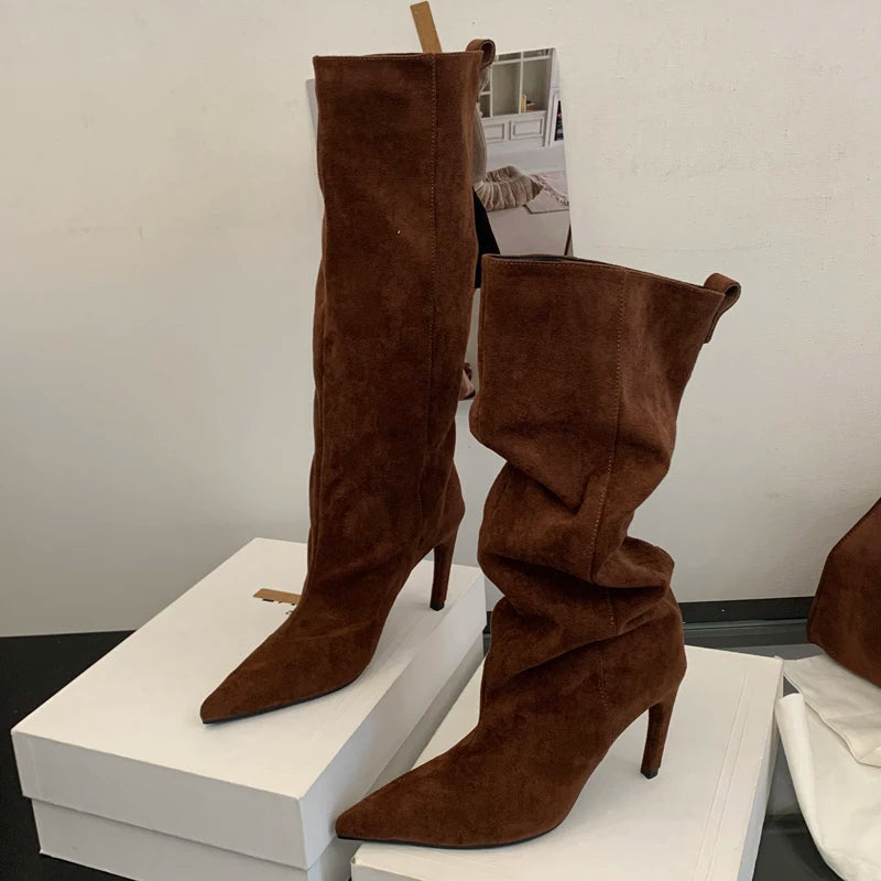 Brown suede knee-high boots on a white platform with a neutral background