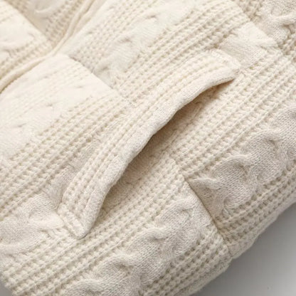 Close-up of a cream-colored knitted blanket with cable pattern on a white background
