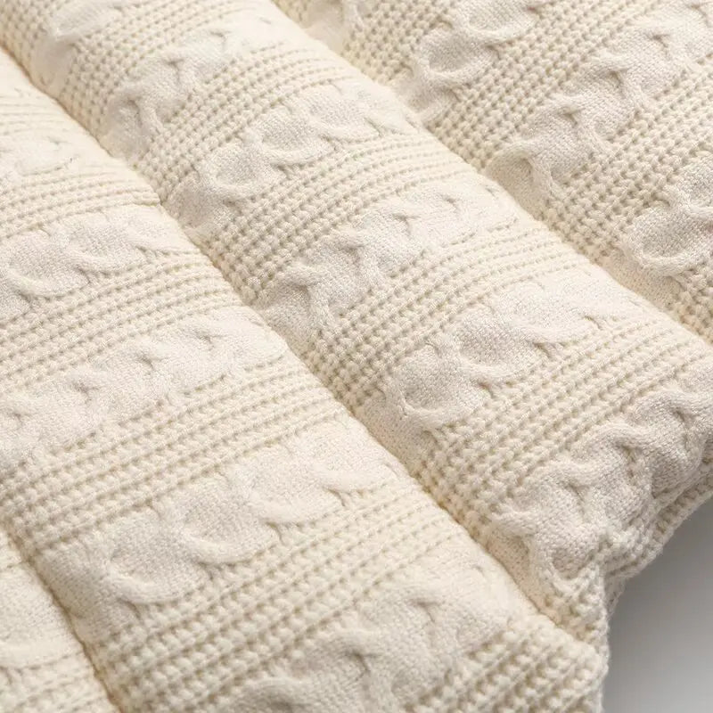 Close-up of a cream-colored textured knit blanket with ribbed and cable-knit patterns.