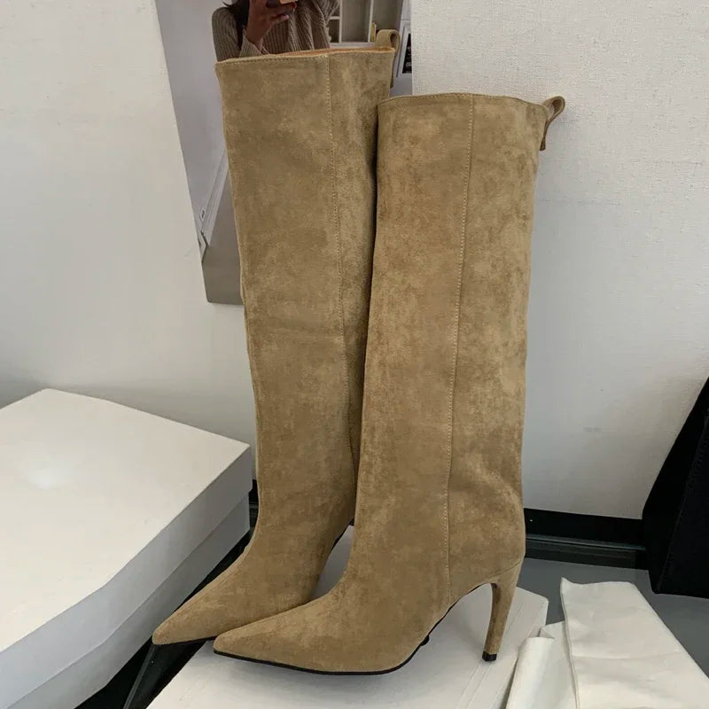 Pair of beige suede knee-high boots on a white surface with a neutral background