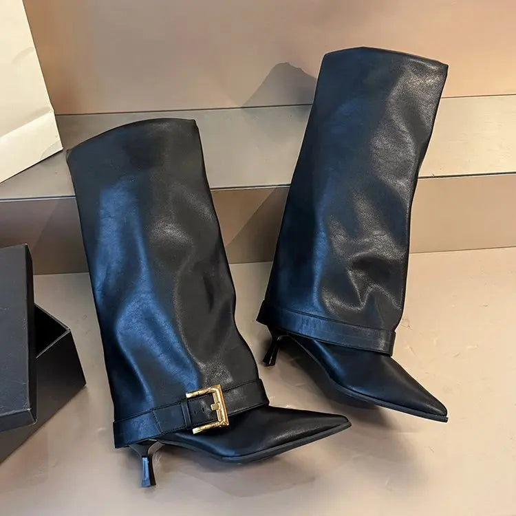 Pair of black leather knee-high boots with a gold buckle on a reflective surface.