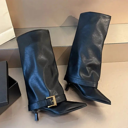 Pair of black leather knee-high boots with a gold buckle on a reflective surface.