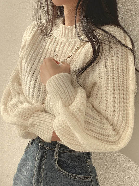 Person wearing a cream knitted sweater and jeans against a neutral background