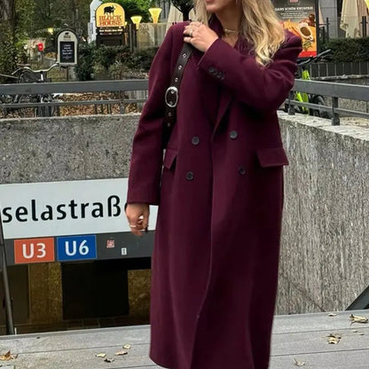 Person wearing a long purple coat standing near a subway sign in an urban setting.