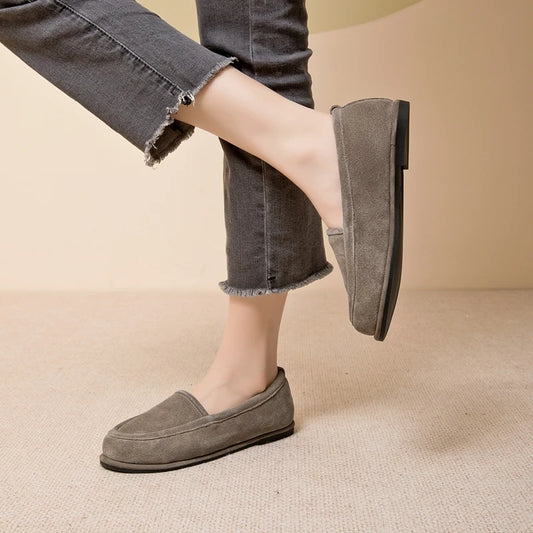 Person wearing gray loafers and dark jeans on a beige background