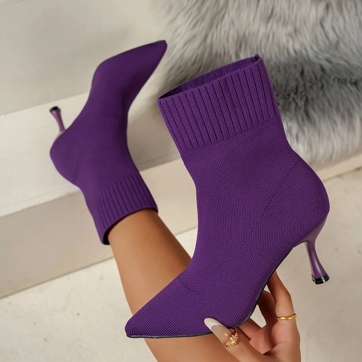 Purple sock boots with high heels held by a person against a neutral background