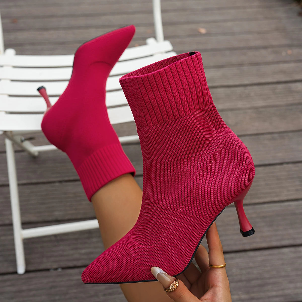 Red high-heeled sock boots being held on a wooden floor.
