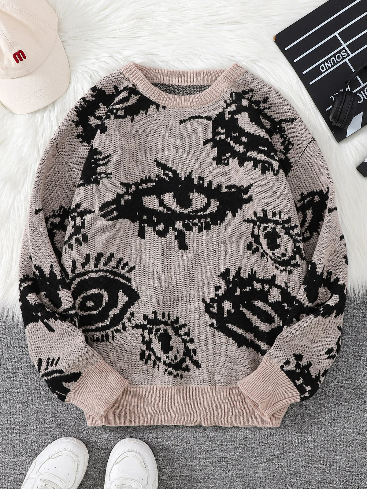 Sweater with eye pattern on a surface with shoes and a cap in the background