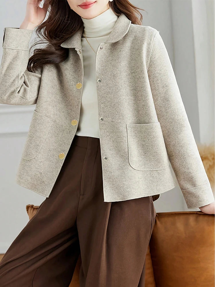 Person wearing a beige jacket and brown pants in a neutral setting