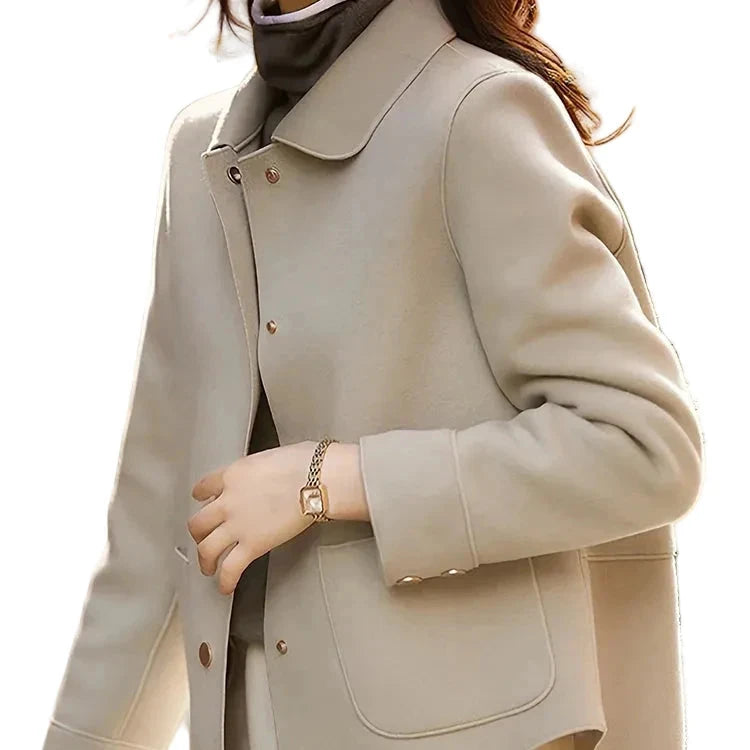 A woman wearing a light beige cropped jacket with a wide collar, button front, and front patch pockets, styled over a dark turtleneck and cream pants against a plain white background.
