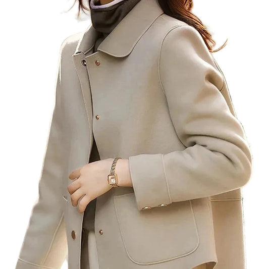 A woman wearing a light beige cropped jacket with a wide collar, button front, and front patch pockets, styled over a dark turtleneck and cream pants against a plain white background.