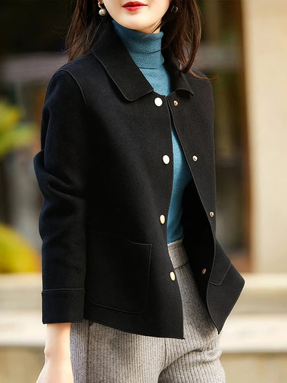 Person wearing a black coat with white buttons, blue sweater, and gray pants.