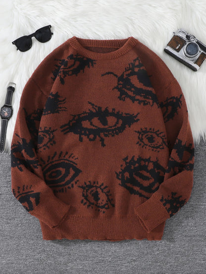 Brown sweater with black eye pattern on a gray surface, surrounded by sunglasses and a camera.