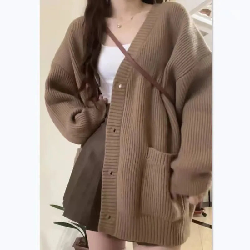 Person wearing a brown cardigan over a white top and dark skirt.
