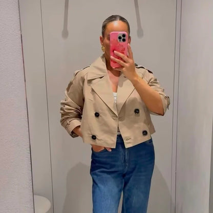 Person wearing a beige trench coat and blue jeans taking a mirror selfie.