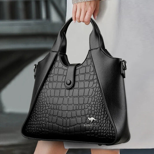 Black handbag with crocodile texture held by a person, blurred background