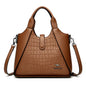 Brown leather handbag with crocodile texture on a white background
