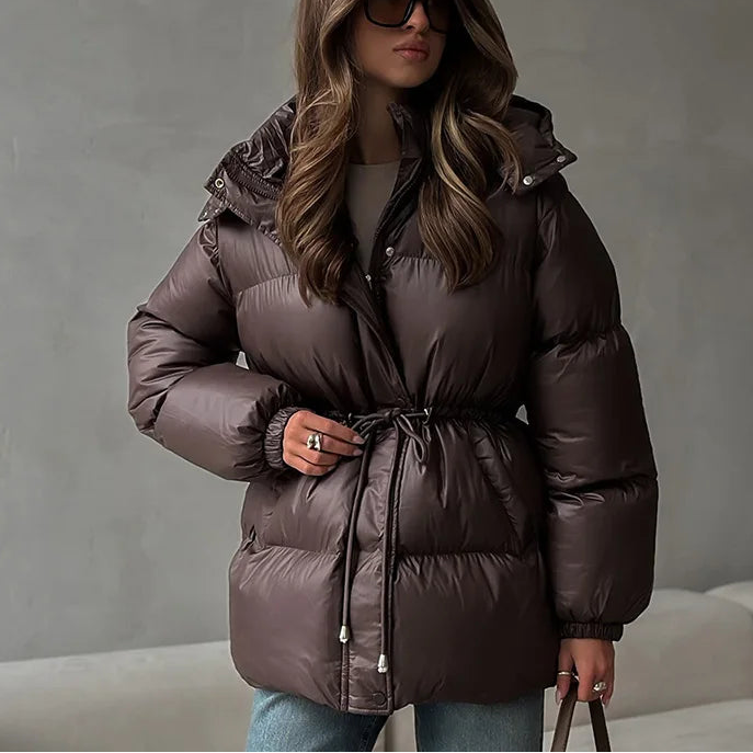 Woman wearing a brown puffer jacket against a gray background