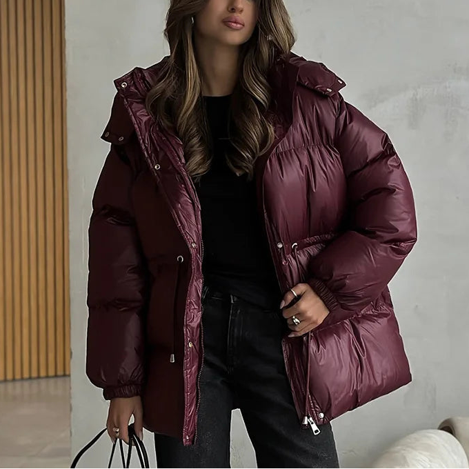 Woman wearing a maroon puffer jacket indoors against a neutral wall.