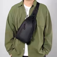 Person wearing a green jacket with a black sling bag on a plain background