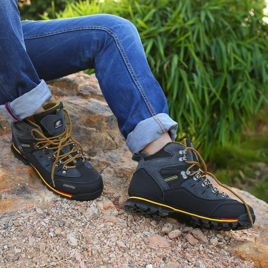 Person wearing black hiking boots with yellow accents on a rocky surface.