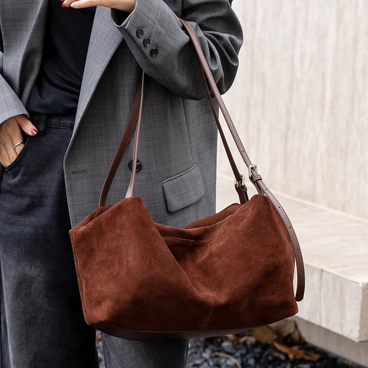 Brown suede handbag held by a person wearing a gray coat and dark pants.