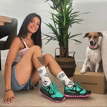 Woman wearing colorful sneakers and socks sitting on the floor with a dog and a box in the background.