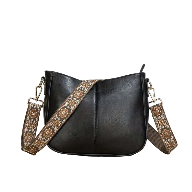 Black handbag with a decorative strap on a wooden surface