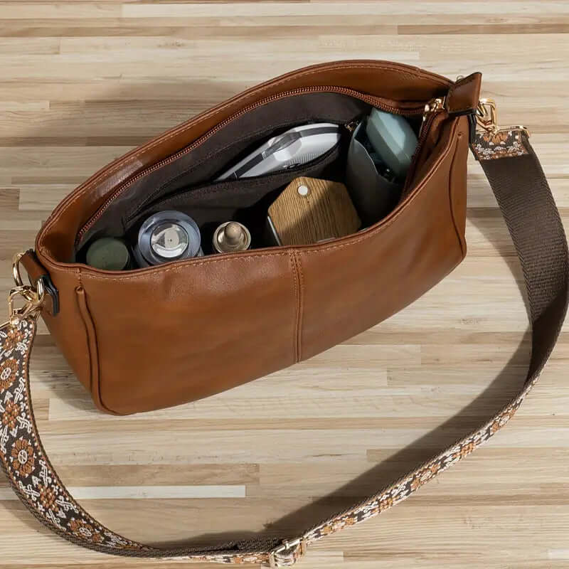 Brown leather handbag with floral strap on a wooden surface