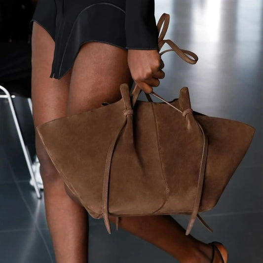 Brown leather handbag held by a person against a blurred background