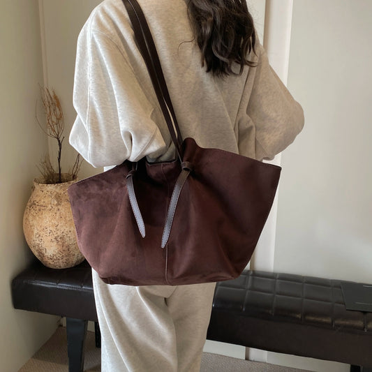 Person holding a brown leather handbag in an indoor setting
