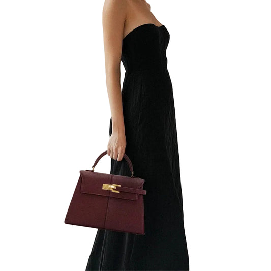 Person holding a burgundy handbag with a gold clasp against a white background