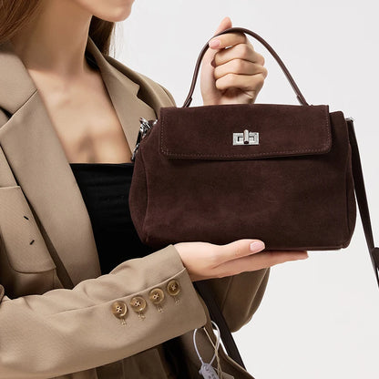 Brown handbag held by a person wearing a beige coat on a light background