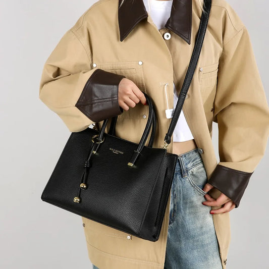 Person holding a black handbag with a plain background
