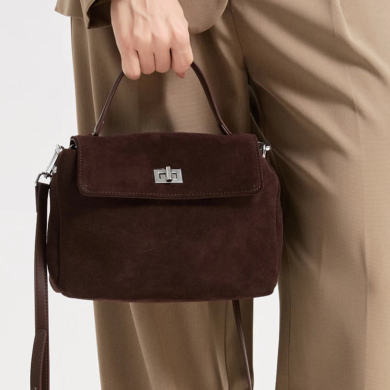 Brown suede handbag held by a person wearing a beige coat on a light gray background