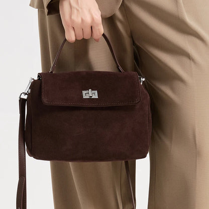 Brown suede handbag held by a person wearing a beige coat on a light gray background